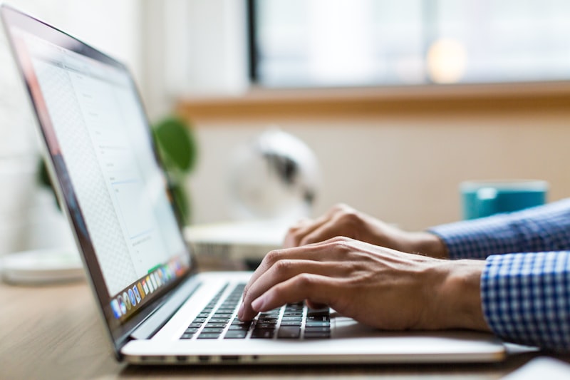Hands typing on a silver laptop at a wooden desk